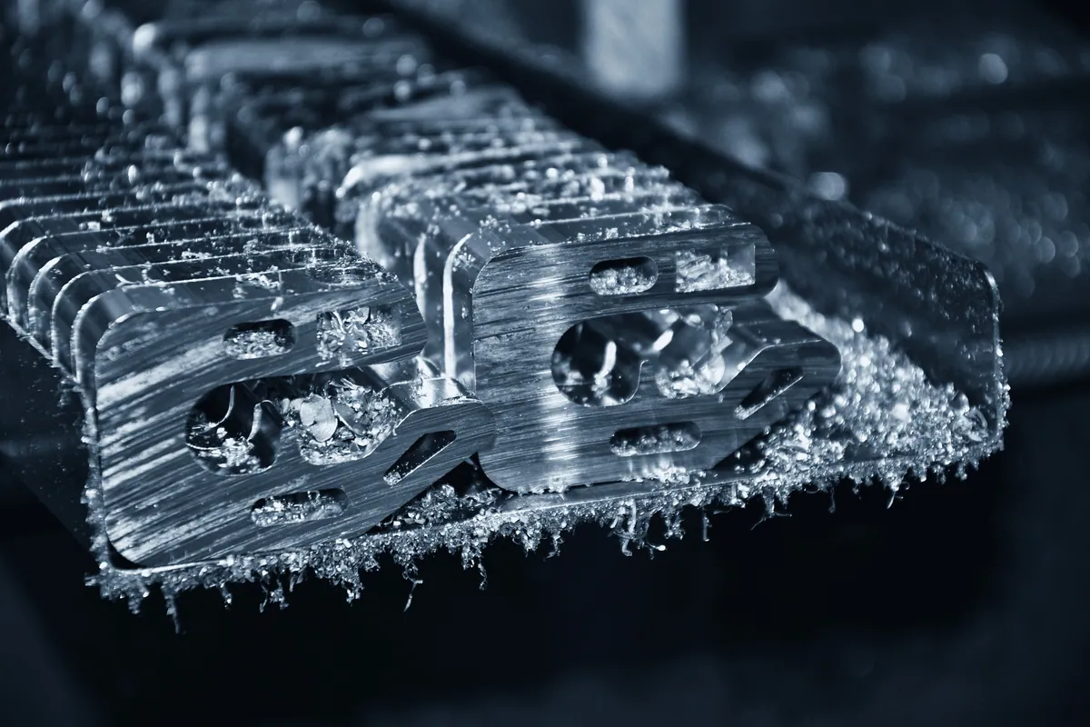 Rij gefreesde aluminium beugels met koelvloeistof en spanen, direct na het frezen van een serie